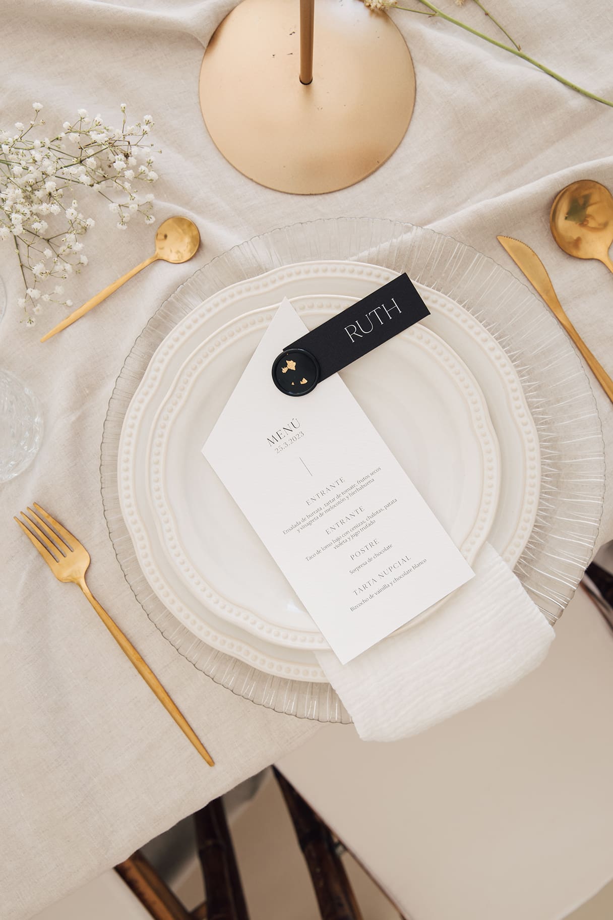 Menú de boda personalizado sobre plato y cubertería dorada en mesa.