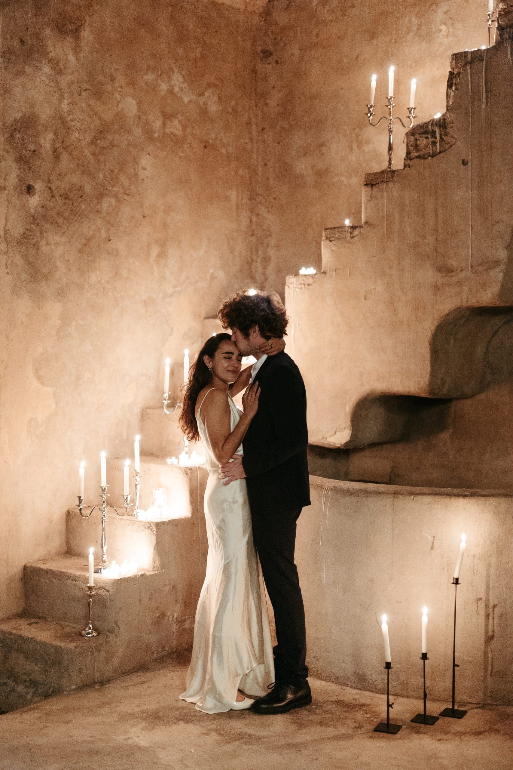 Novios abrazándose bajo la suave iluminación de velas dispuestas en una escalera, en un momento de intimidad y romance. Momento organizado por wedding planner de Bouclé Weddings.