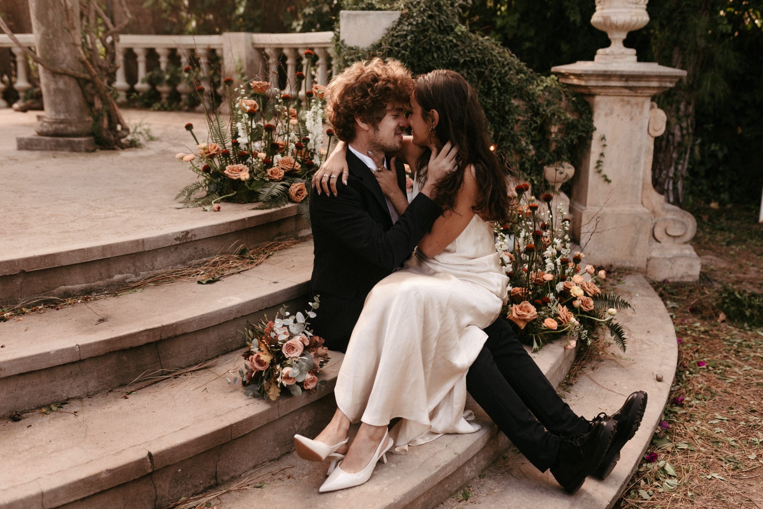 Romántico beso de los novios en las escaleras de un altar decorado con flores y candelabros.