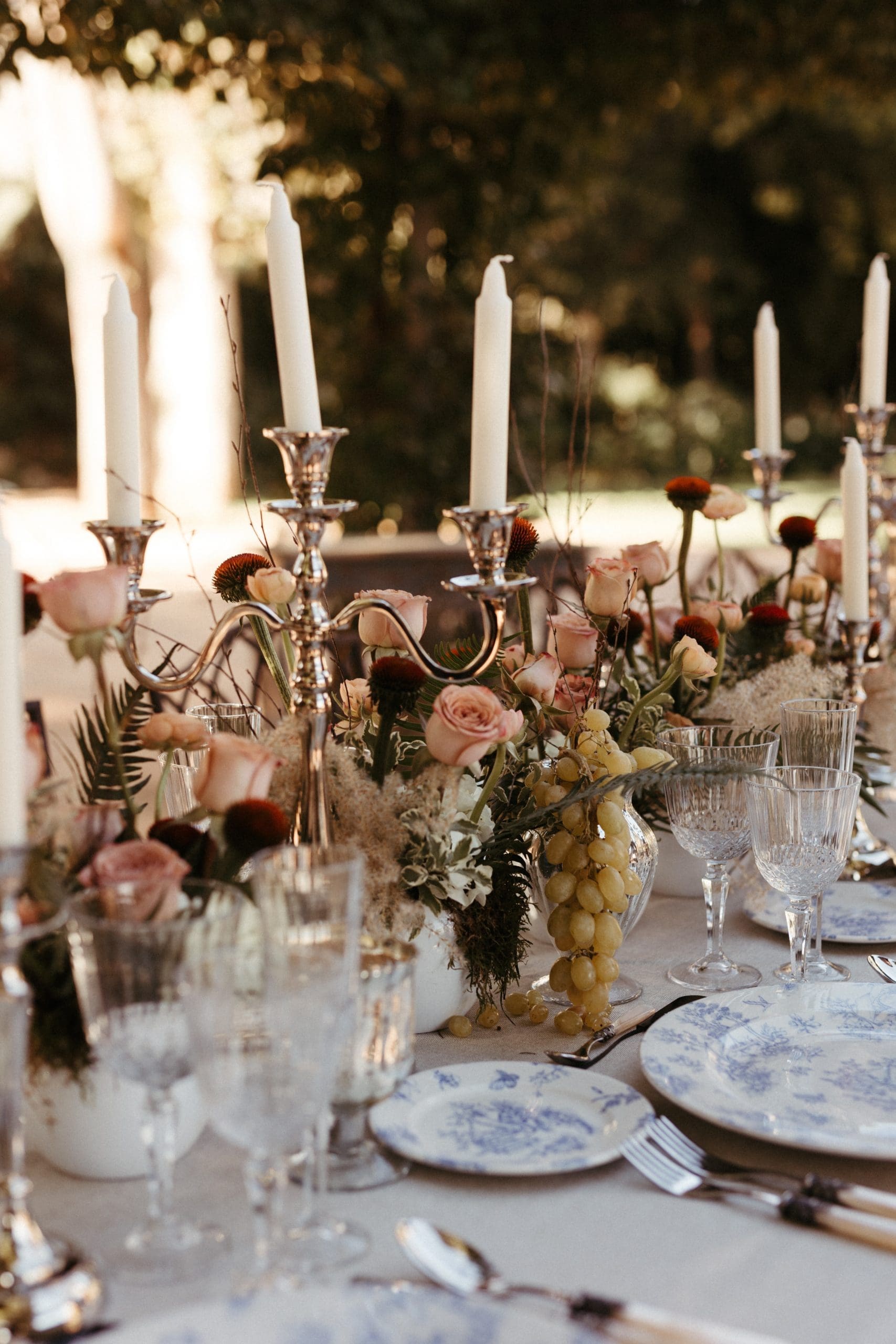 Mesa de bodas en Casa Santonja, Alicante, con candelabros, uvas, velas y vajilla toile de jouy bajo la luz de un atardecer romántico. Creada por wedding planner de Bouclé Weddings.