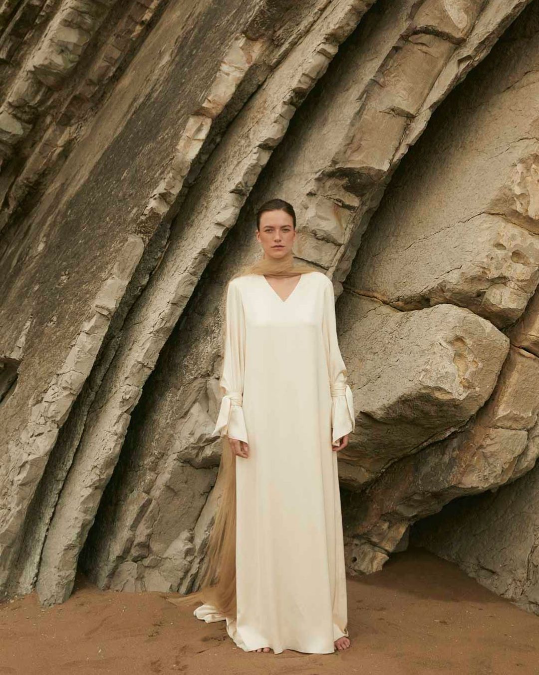 Modelo luciendo un vestido de novia de Claudia Llagostera, con una imponente pared rocosa de fondo.