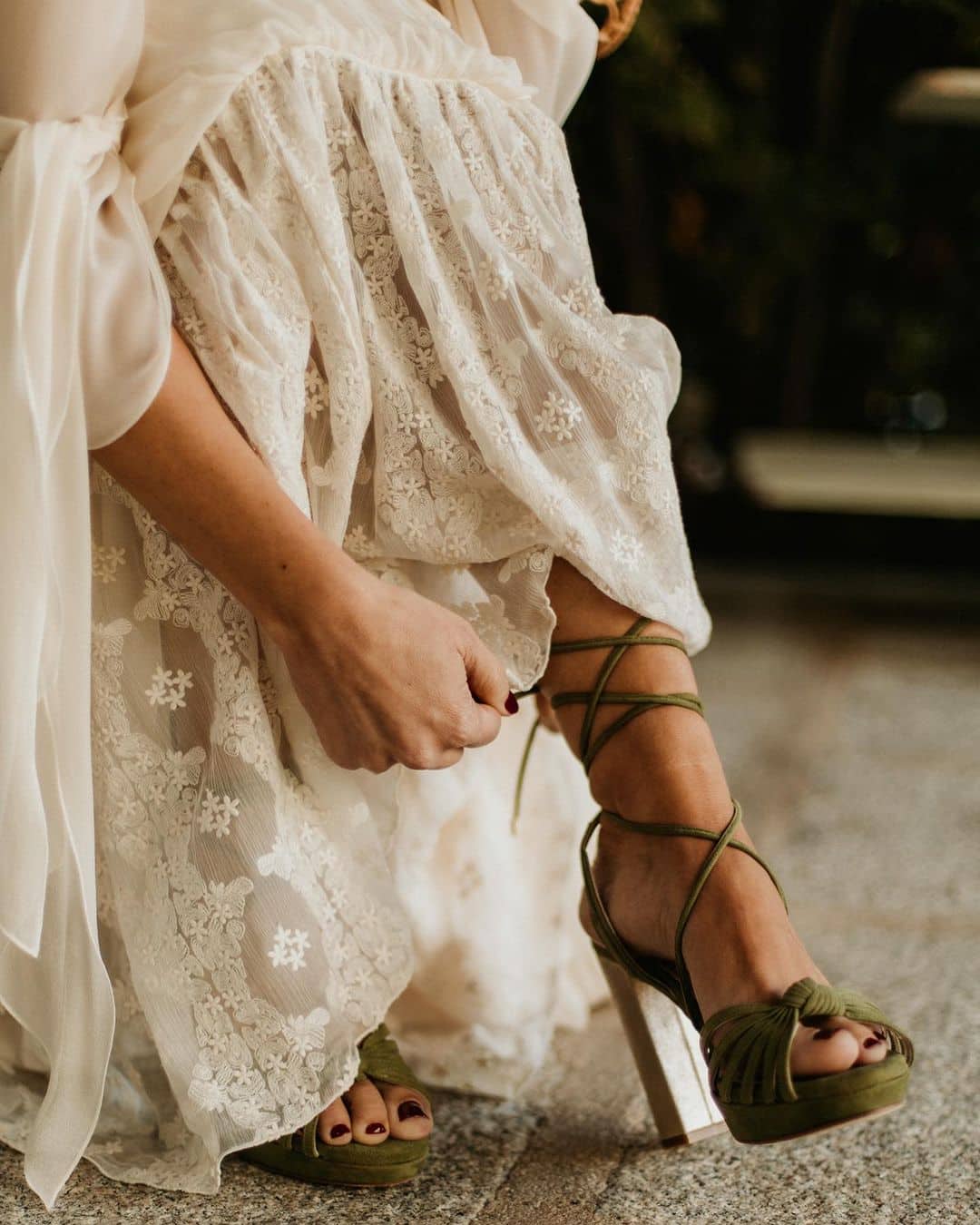 Novia ajustando su zapato con detalle de la falda de un vestido diseñado por Claudia Llagostera visible.