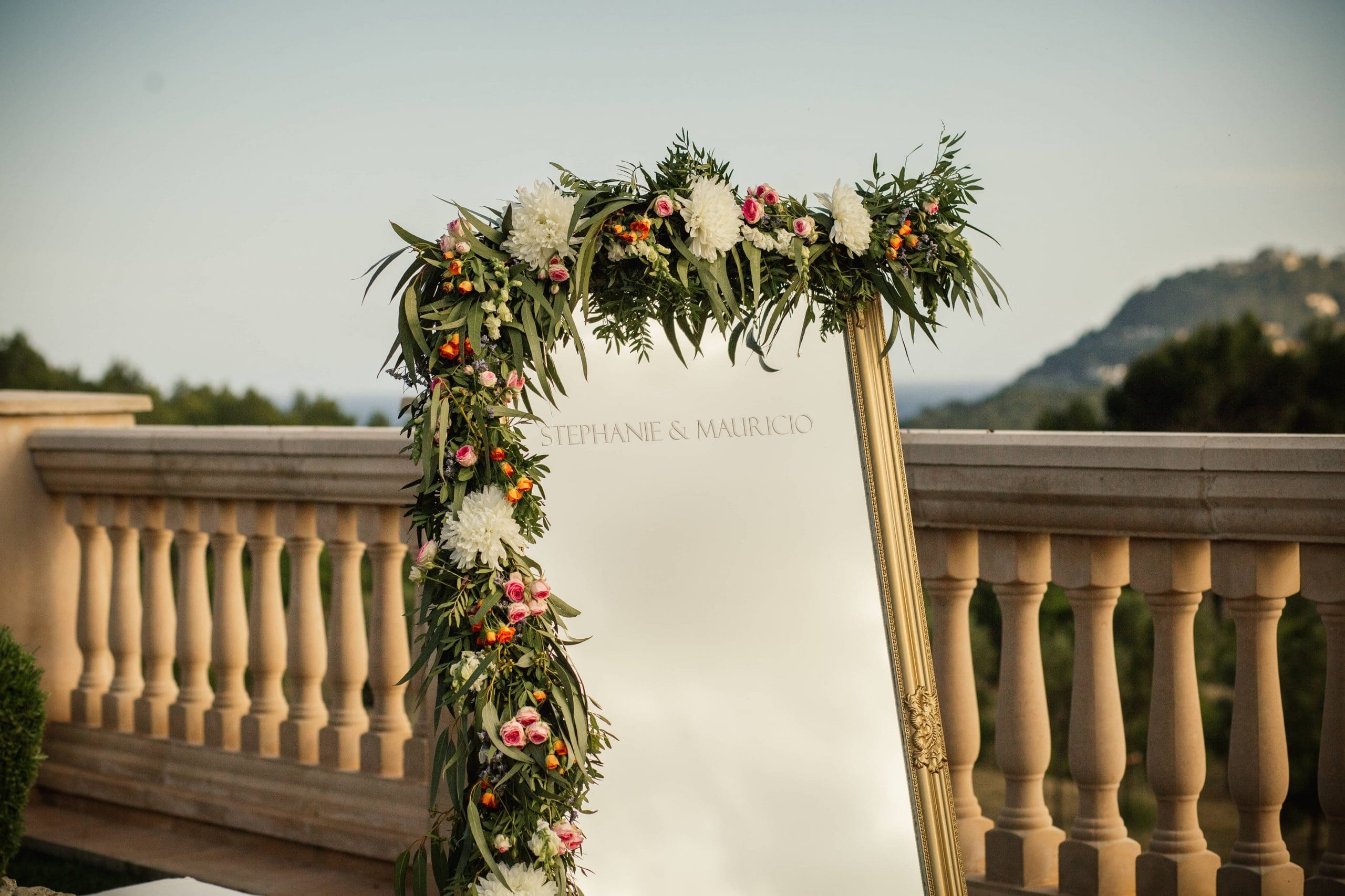 Espejo decorado con flores en su marco, con los nombres de los novios grabados, reflejando una boda en Mallorca.