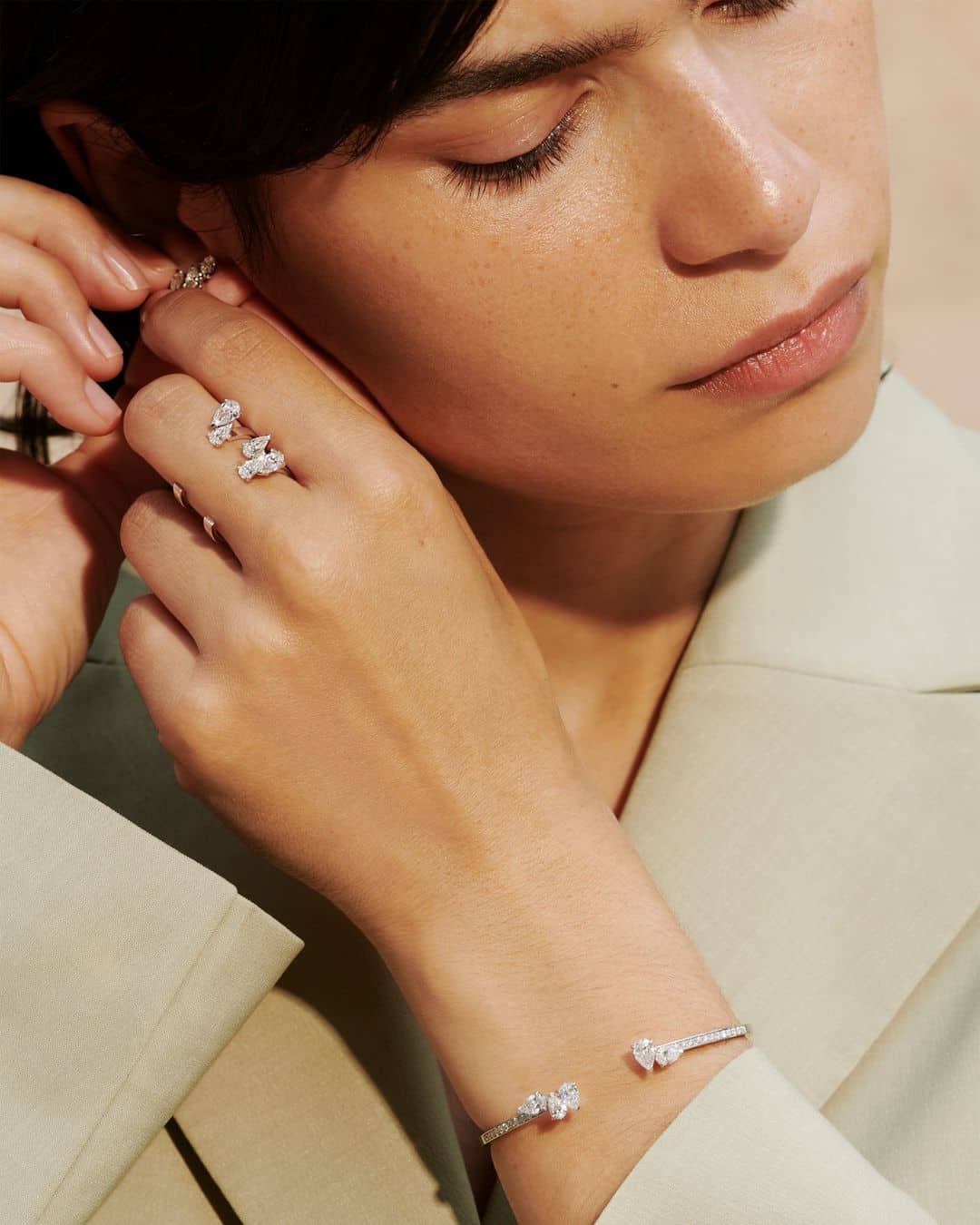 Mujer colocándose pendientes de Repossi mientras luce anillo de compromiso abierto de diamantes y brazalete a juego