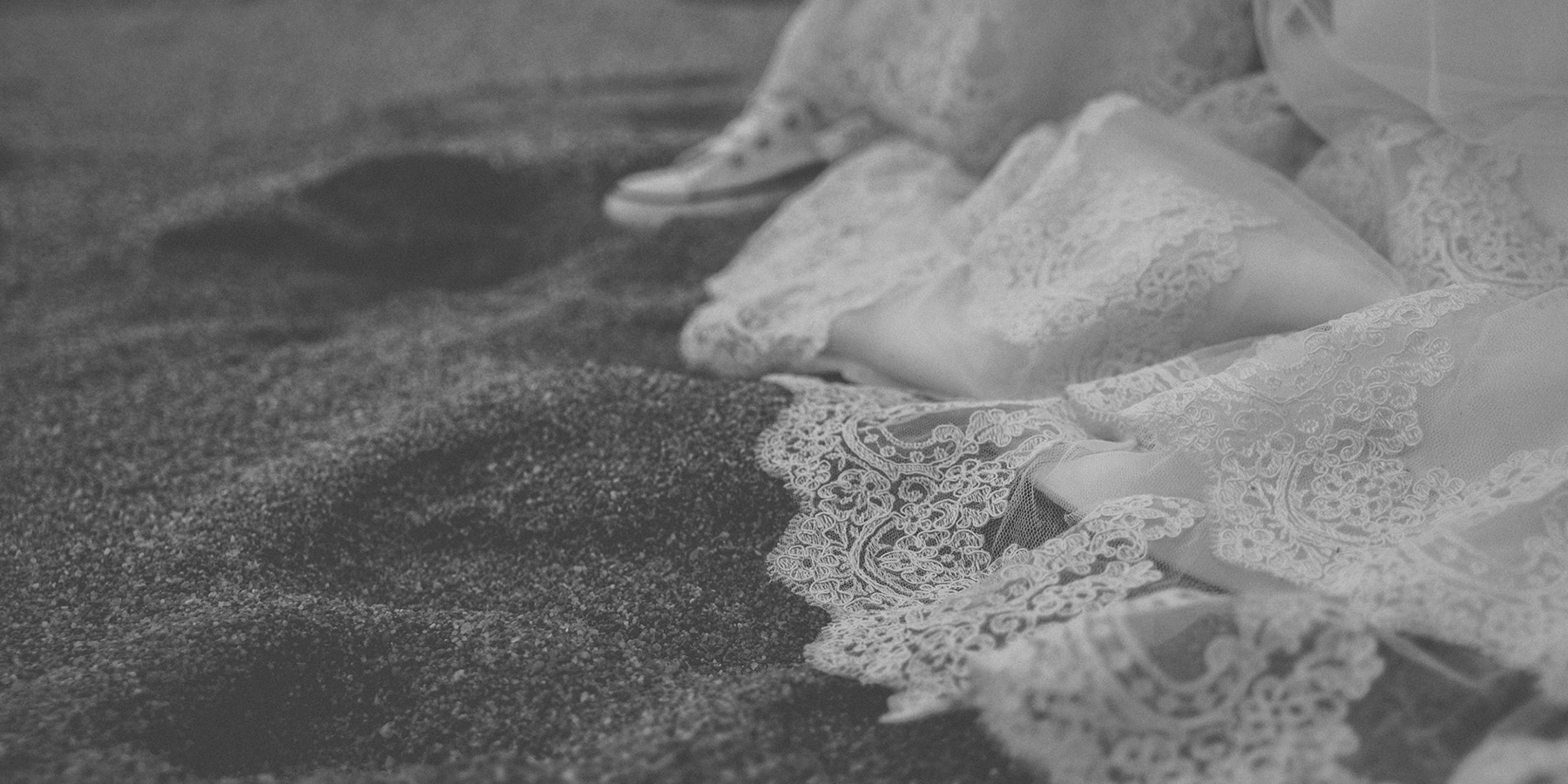 Detalles de la cola de un vestido de novia arrastrándose por la arena.