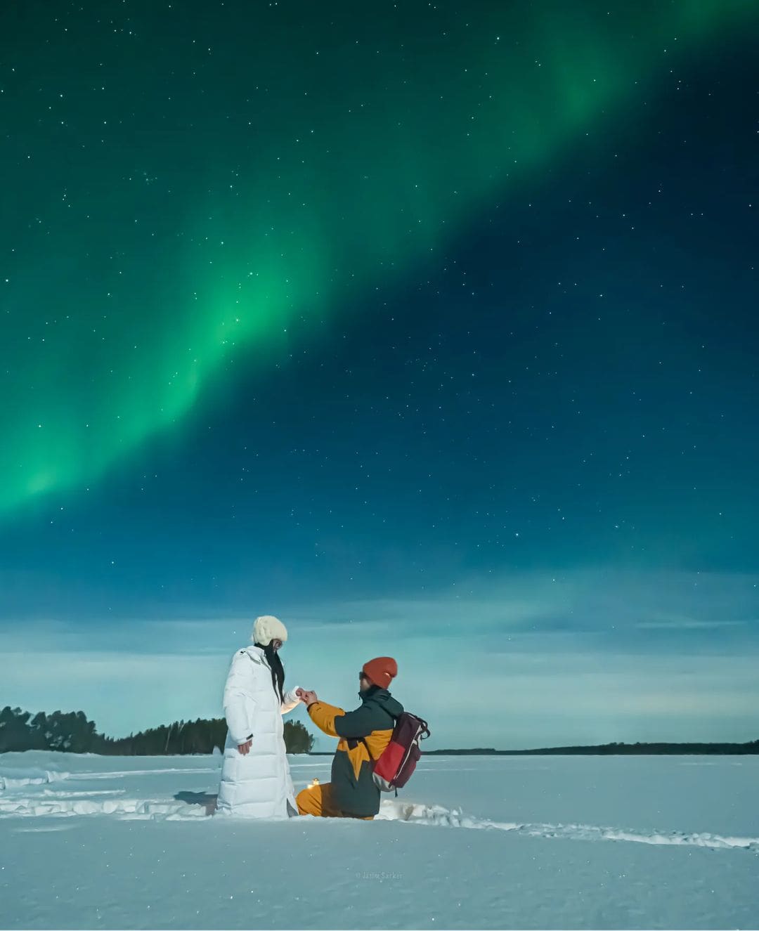 Hombre arrodillado en la nieve pidiendo matrimonio a su mujer en Laponia bajo la aurora boreal, momento de luna de miel