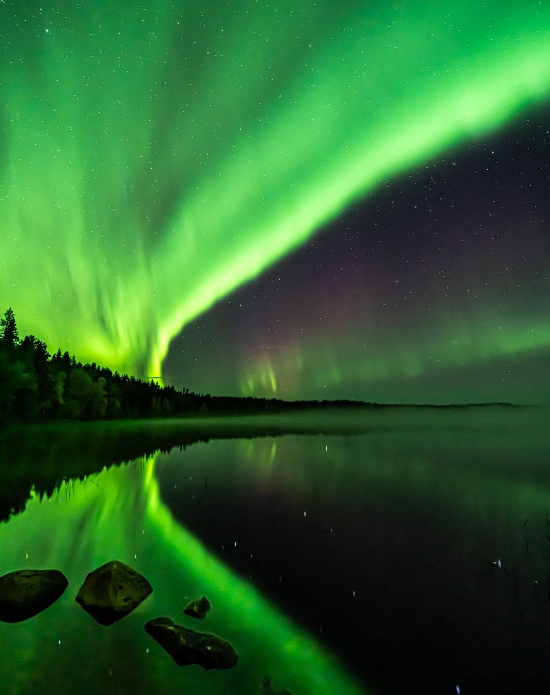 Lago reflejando una aurora boreal verde en Laponia, escenario romántico para la luna de miel
