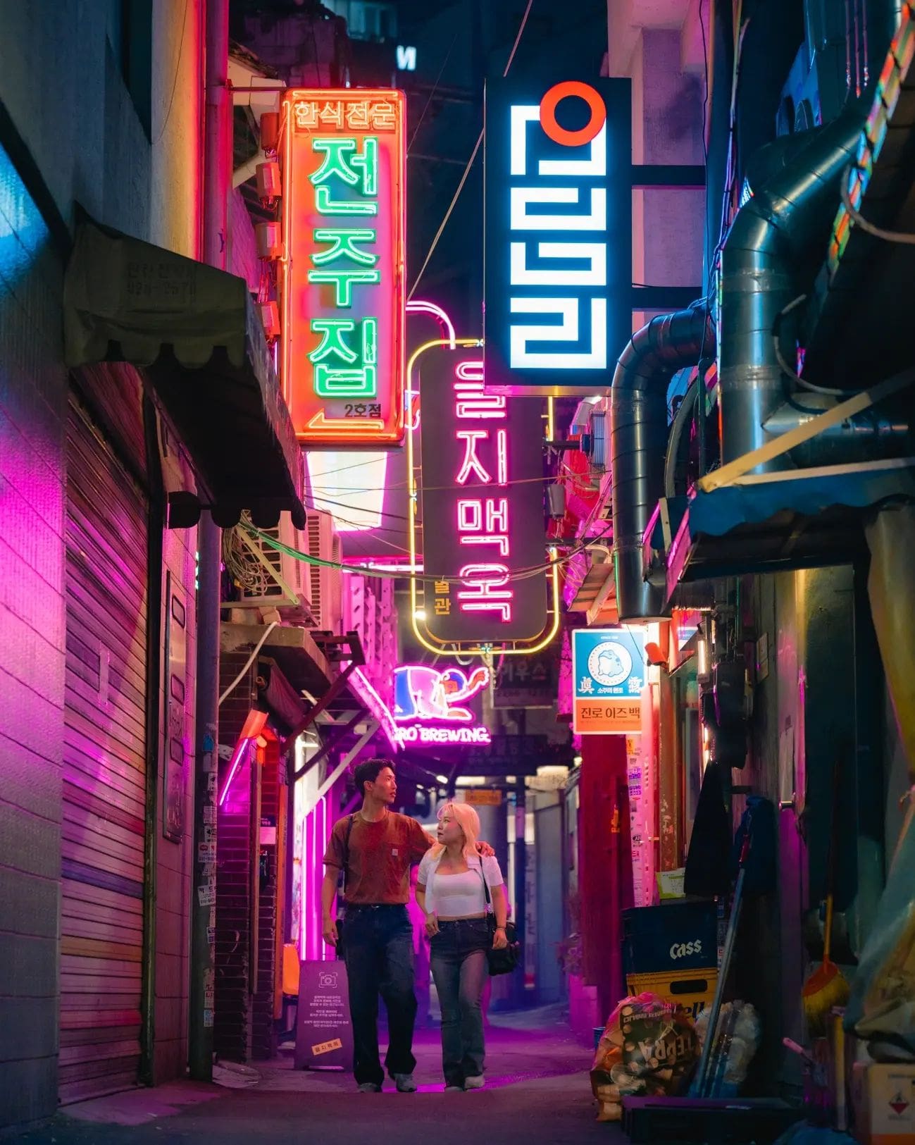 Pareja en luna de miel paseando por una calle estrecha con letreros luminosos en Seúl
