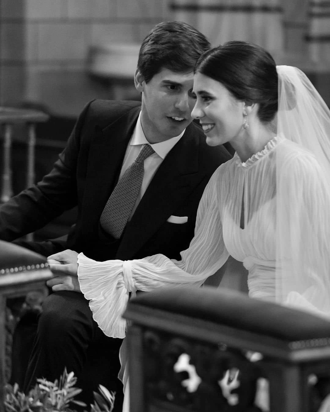 Novio susurrando al oído de la novia mientras están sentados frente al altar durante el rito de la velación - Bouclé Weddings