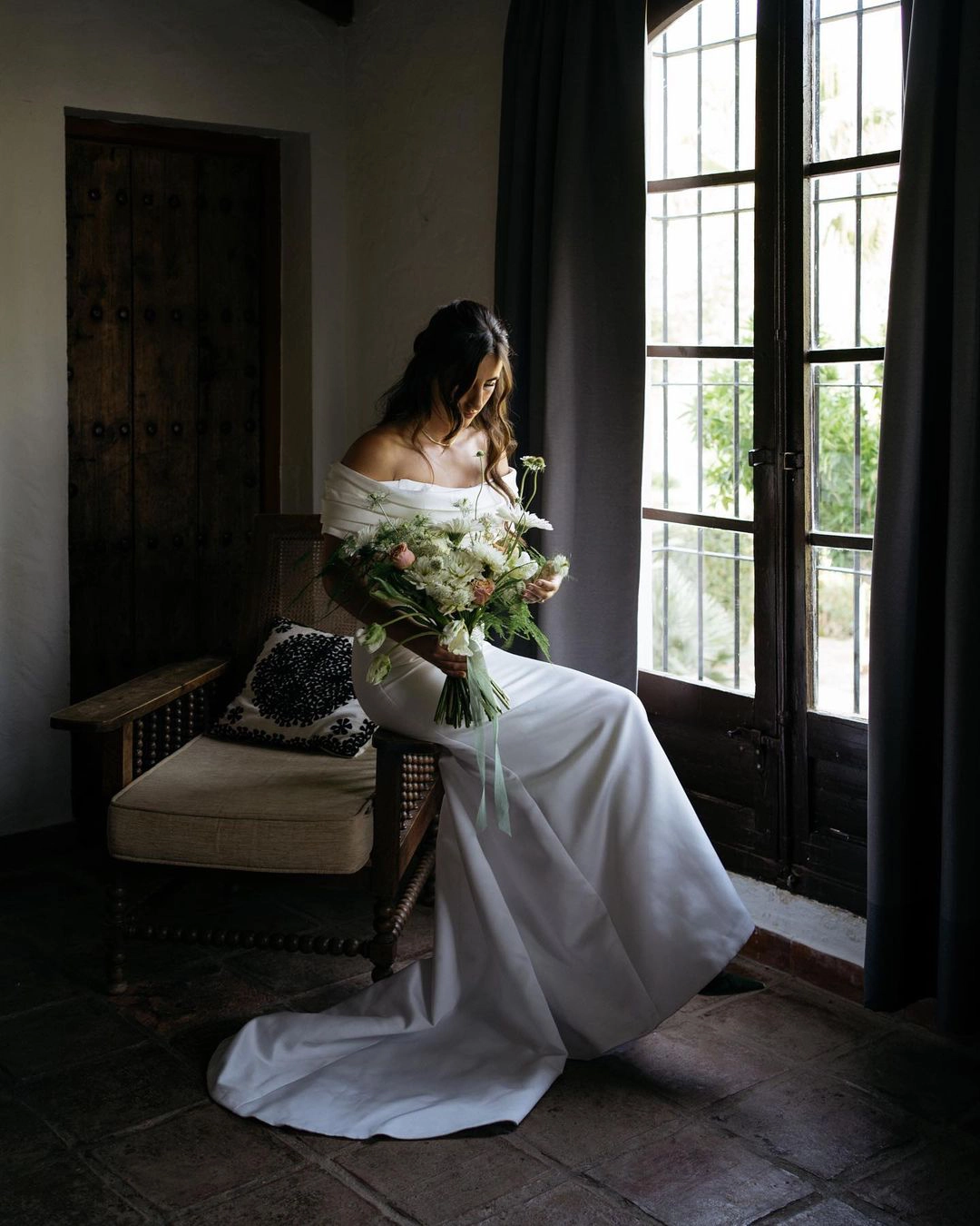 Novia sentada sosteniendo y observando su ramo de flores, en un momento de introspección sobre sus votos de boda.