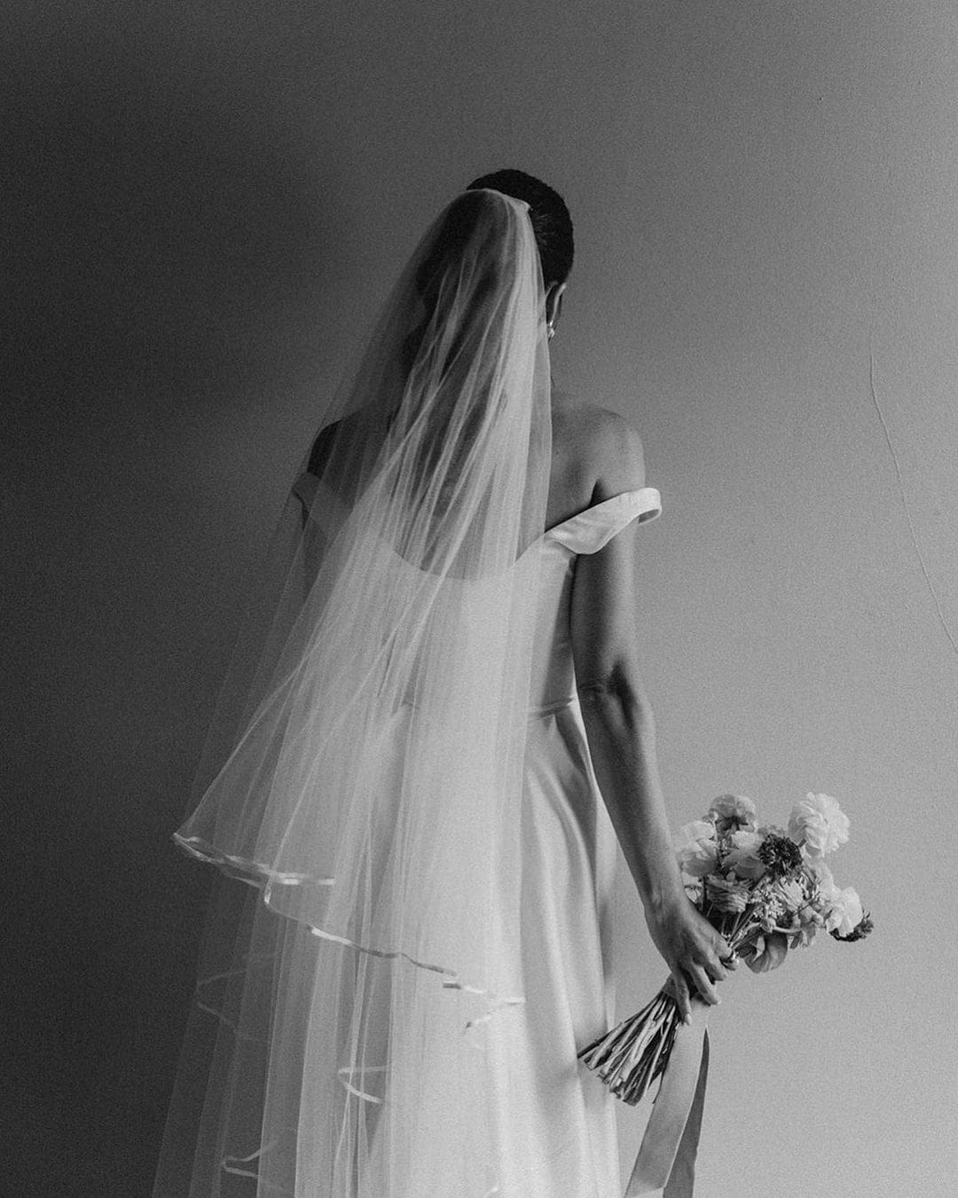 Novia de espaldas sosteniendo un ramo de novia en la mano derecha, enfrentando nervios antes de la boda