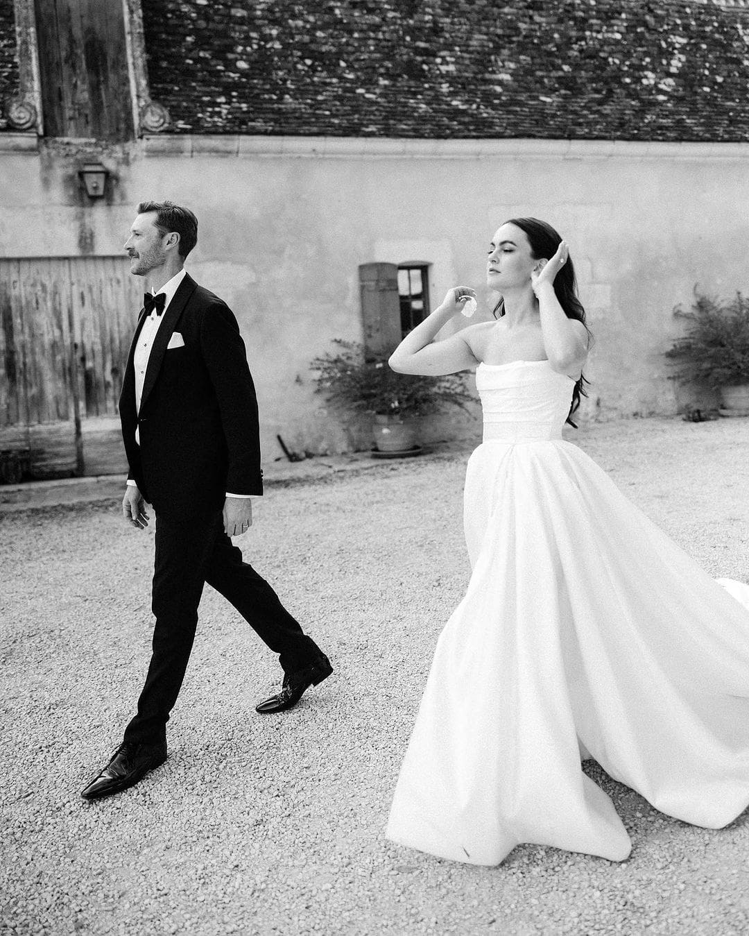 Novios caminando juntos en blanco y negro, con la novia recogiéndose el pelo.