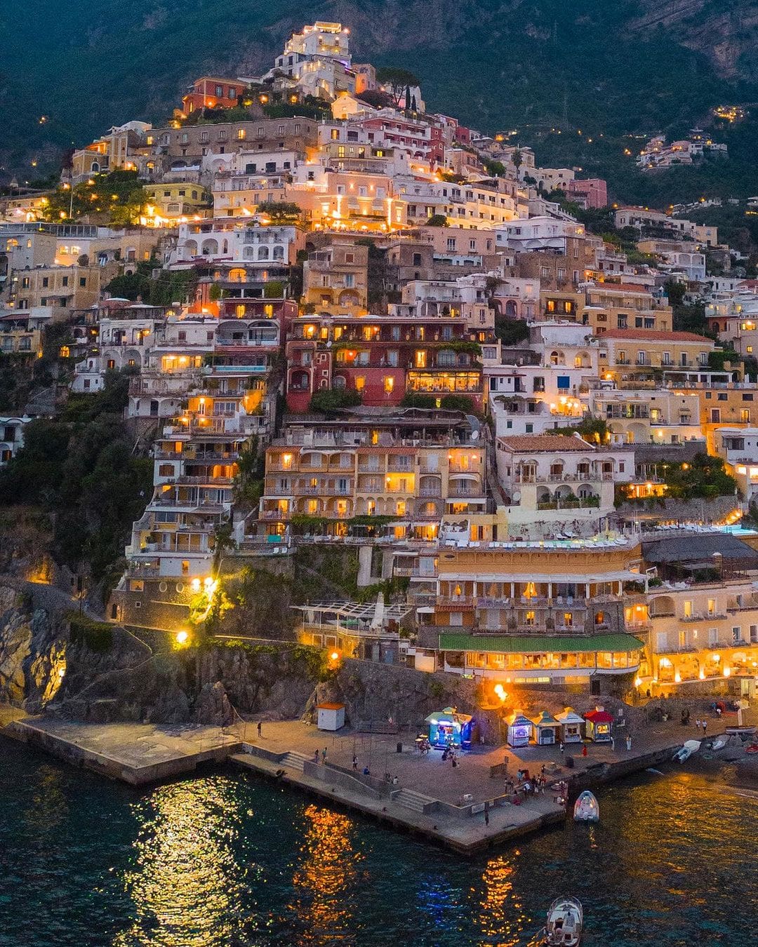 Vista nocturna de la Costa Amalfitana con luces centelleantes a lo largo de la costa, reflejando un paisaje marino encantador y un ambiente vibrante."