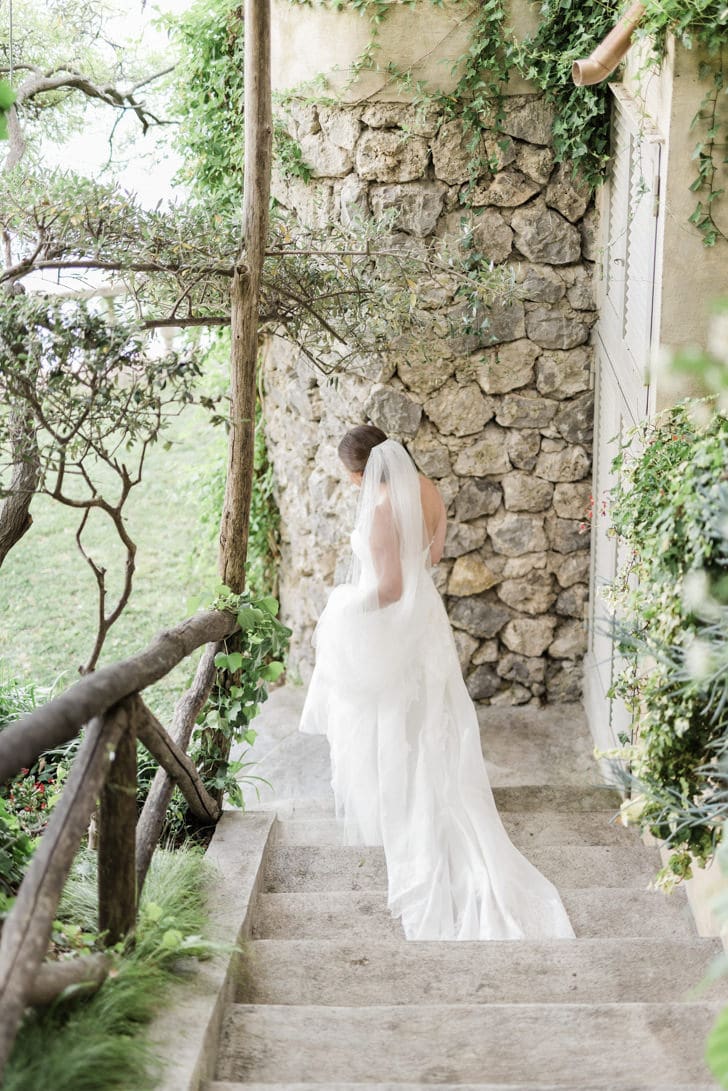 Una novia elegante caminando por los jardines del Hotel Santa Caterina, con el esplendor de la Costa Amalfitana de fondo.