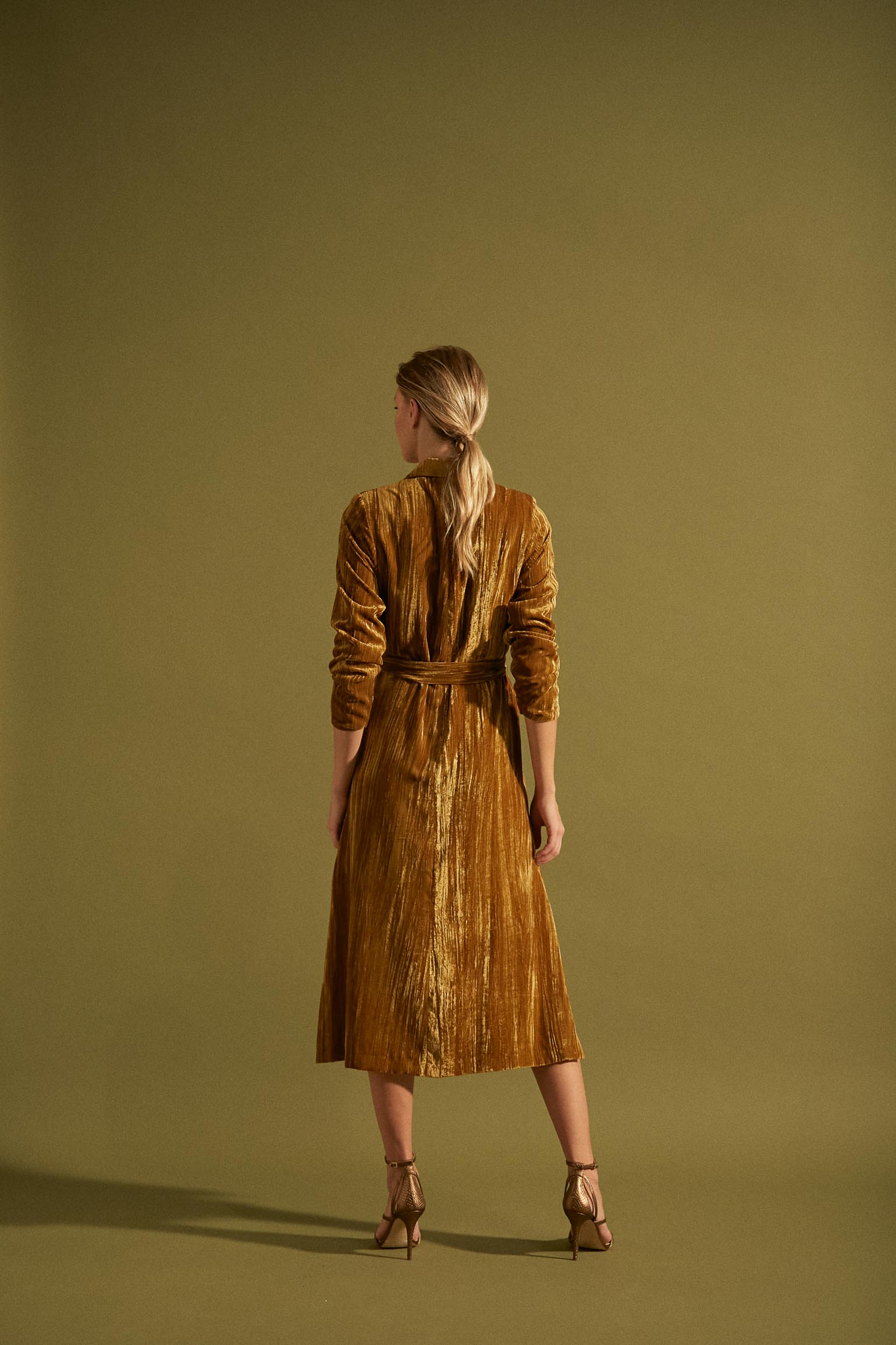 Vista trasera del Vestido Kannon de Bimani en terciopelo 'velvet gold', enfocando su diseño elegante con cinturón y aberturas laterales.