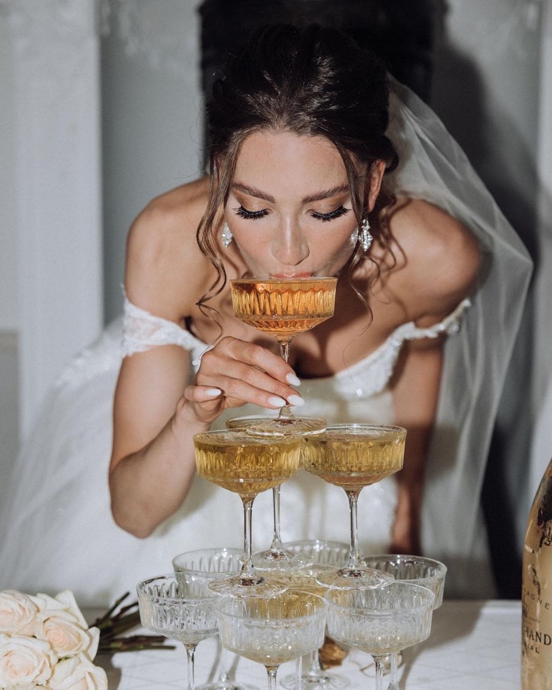 Novia disfrutando de un sorbo de champán de una elegante torre de copas en su boda, celebrando su compromiso y felicidad