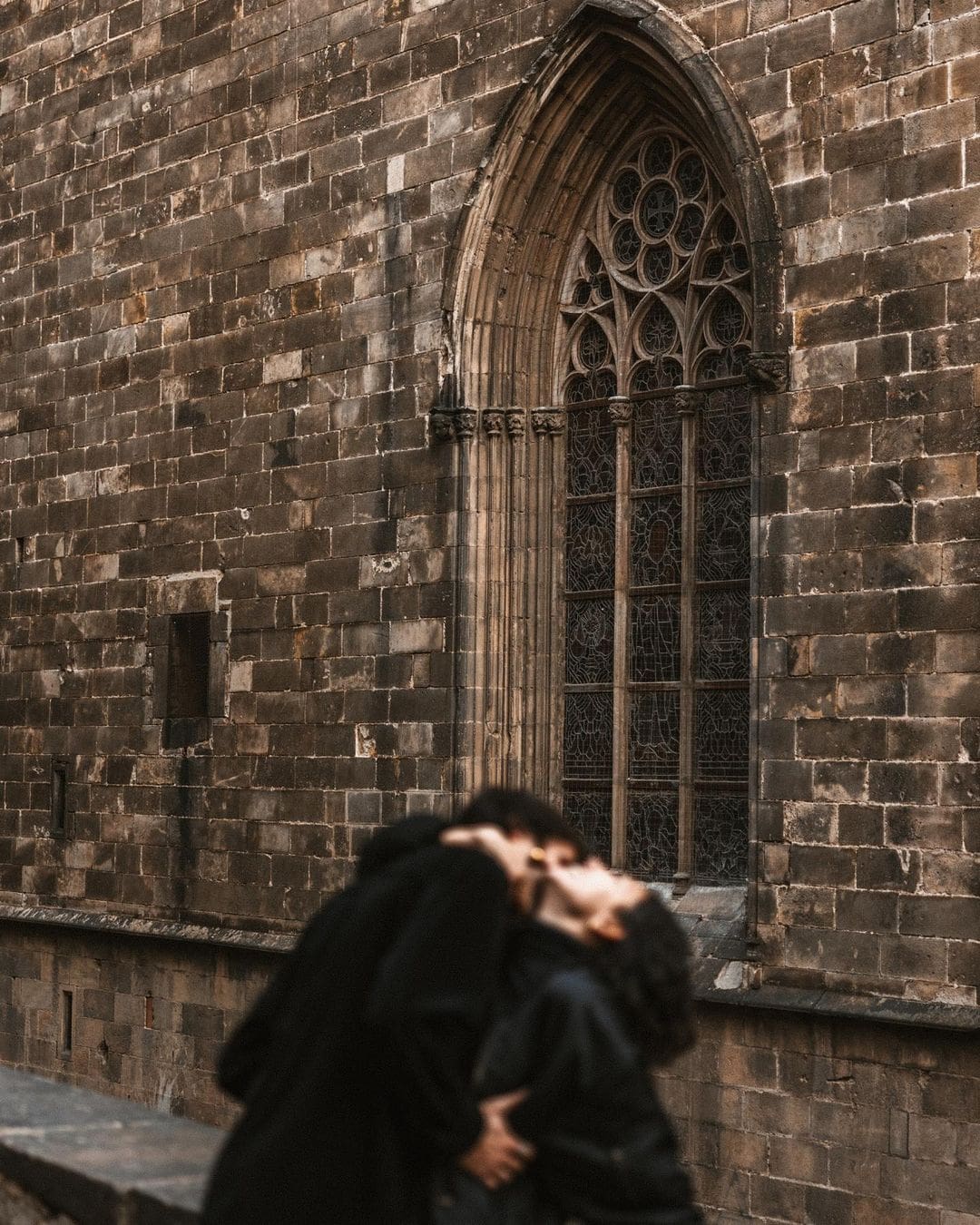 Pareja compartiendo un beso en el cuello, con la ventana de una iglesia gótica al fondo, simbolizando un amor eterno en San Valentín.