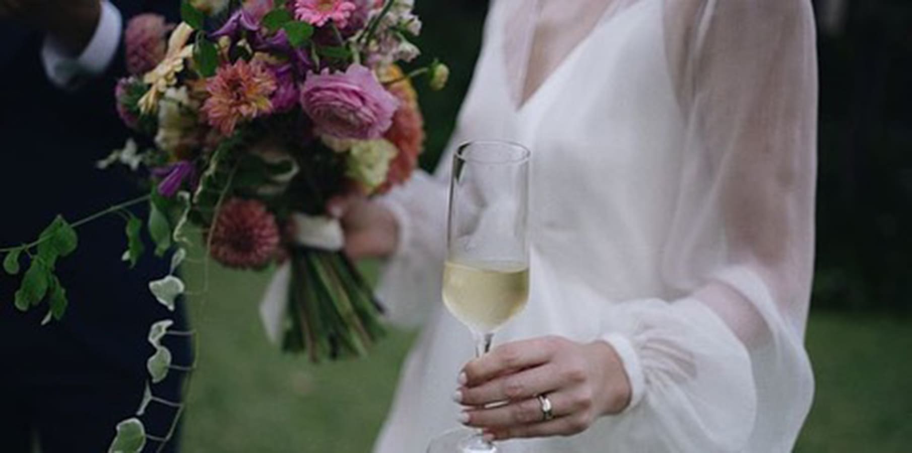 The bride holds her bridal bouquet in one hand and a champagne glass in the other with grace.
