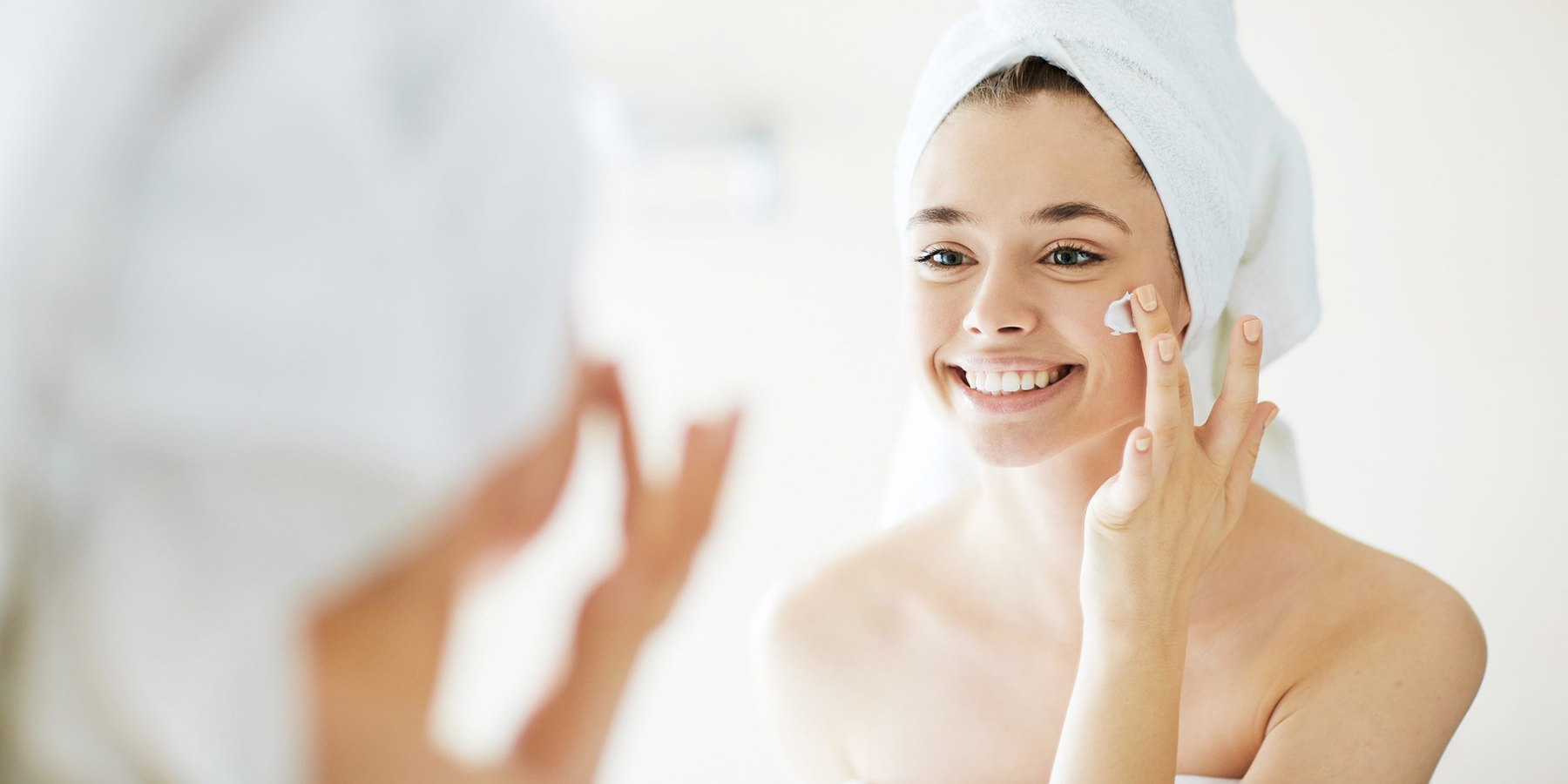 Novia aplicando crema facial frente al espejo como parte de su rutina de cuidado de la piel antes de la boda.