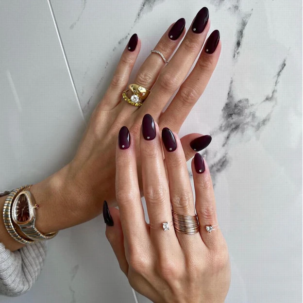 Detalle de uñas con manicura en tonos burdeos, perfectas para una boda, con acabado elegante y distintivo.