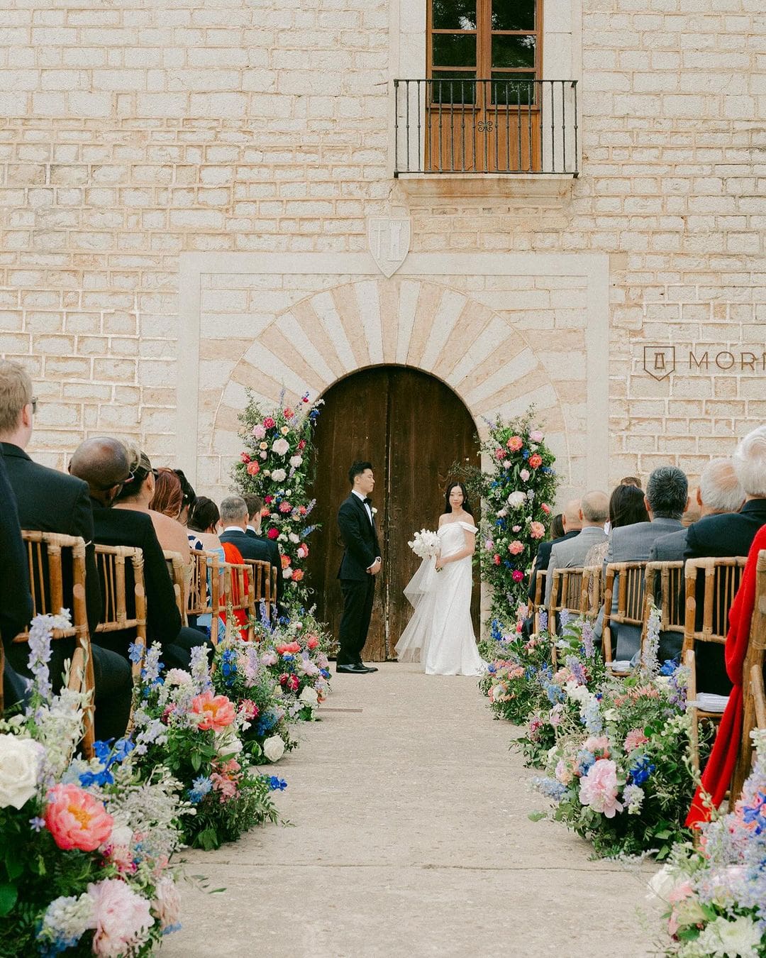 Ceremonia de boda al aire libre con los novios frente a una puerta adornada con flores, simbolizando el cordón rojo del destino.