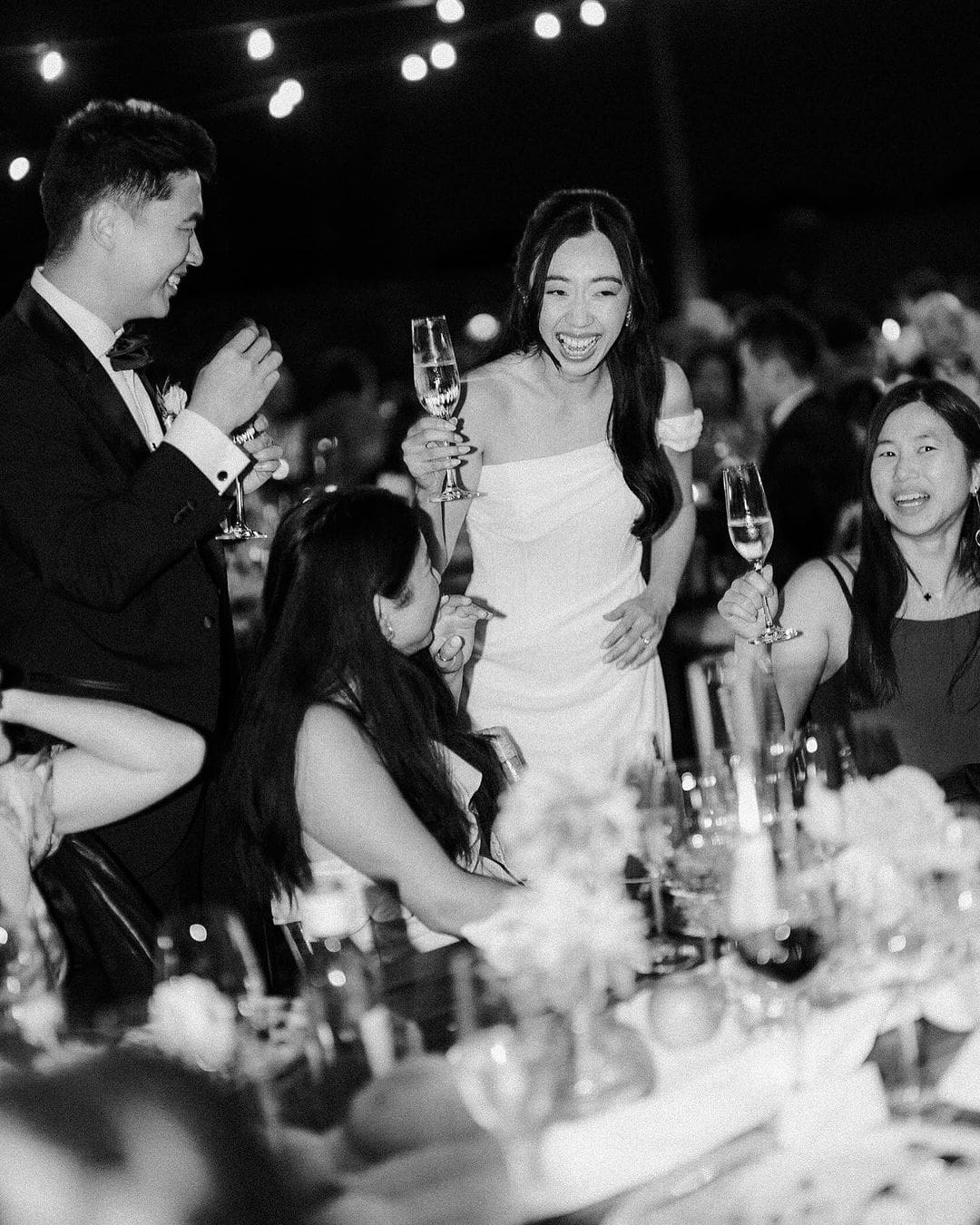 Novios brindando con amigos en la recepción de boda, celebrando su conexión con el hilo rojo del destino.