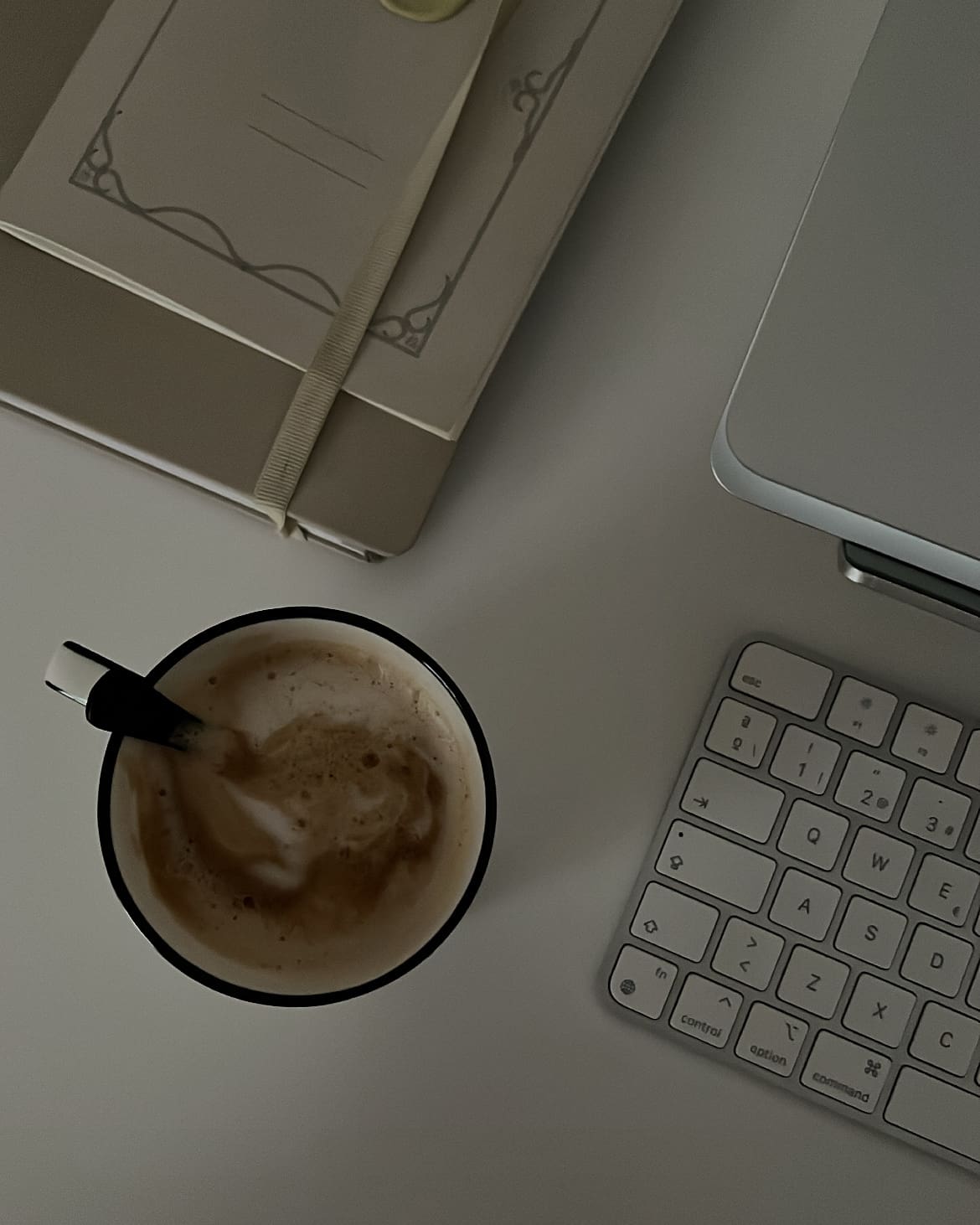Taza de café con espuma junto a un cuaderno y un teclado sobre un escritorio, parte de una rutina de mañanas productiva.