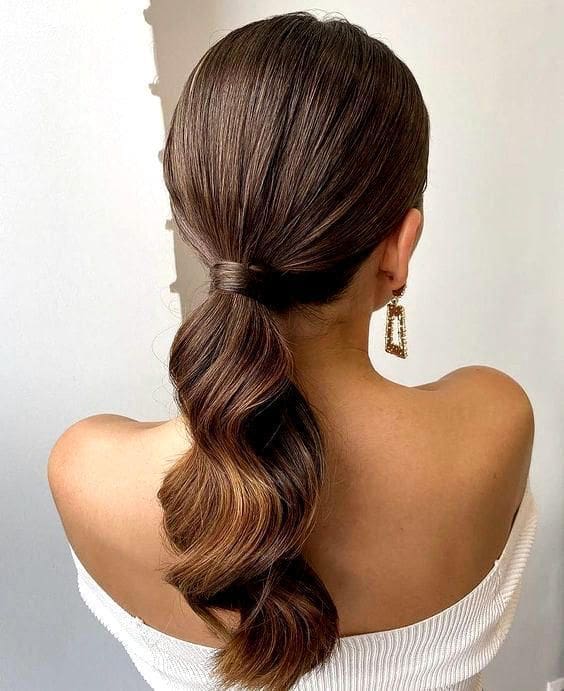 Coleta baja elegante con raya en medio o mechones sueltos para invitadas de boda.