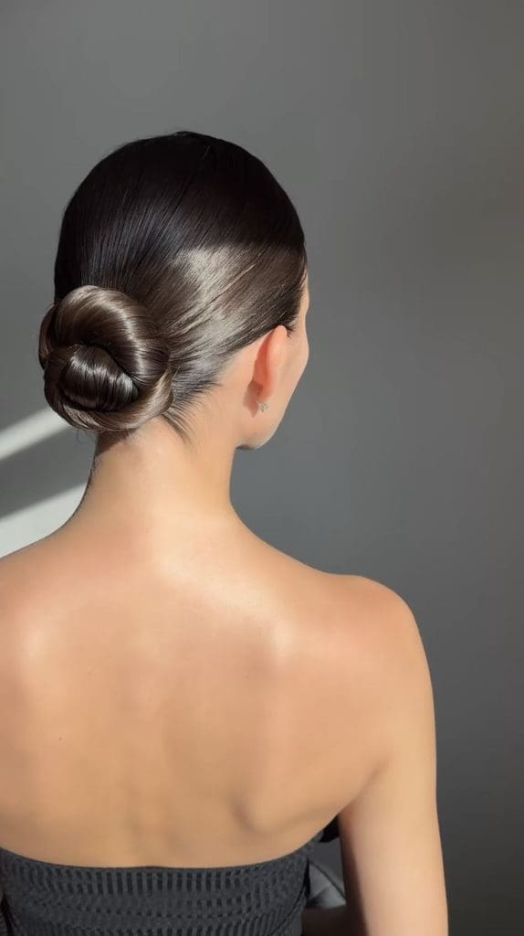 Moño de bailarina elegante para invitadas de boda con recogido alto y pulido.